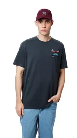 Remera blanca de algodón orgánico con cuello redondo y manga corta. Presenta un estampado en el pecho con una cruz formada por dos tablas de surf en tonos rojo, azul y negro.