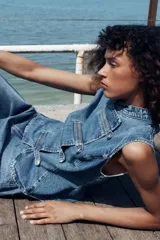 Top de denim blanco sin mangas, con cuello mao y cierre frontal cruzado con trabillas y botones metálicos.