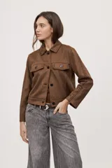 Campera negra de efecto gamuzado con cuello camisero, cierre frontal de botones, bolsillos plaqué en el pecho y detalles de costuras decorativas y calados.