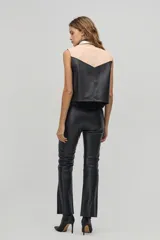 Chaleco de cuero negro y beige con cuello camisero, sin mangas y cierre frontal con botones a presión. Diseño con canesú en contraste y corte recto.