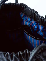 Bolso tipo tote bag de cuero negro, con diseño fruncido en la parte superior y dos asas delgadas de hombro. Presenta un acabado de cuero suave y arrugado.
