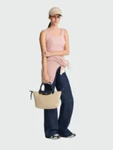 Cartera de mano modelo Le Pliage Energy de Longchamp, tamaño S. Presenta un diseño estructurado en color beige con detalles en negro, incluyendo asas cortas, solapa frontal con cierre de botón a presión y correa lateral con cordón.