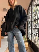 Campera tipo hoodie de textura tipo corderito en color negro, con diseño de collage en la espalda que combina parches en tonos marrón, blanco y estampado animal print de leopardo.