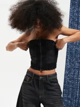 Top tipo corset confeccionado en denim negro, con escote strapless y cierre frontal con cremallera.