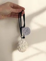 Collar con dije circular de gran tamaño con textura martillada en acabado plateado, montado sobre una tira de cuero negra regulable.