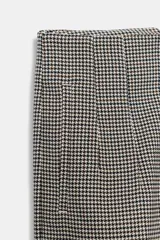 Pantalón tobillero de tiro alto con estampado de cuadros pequeños en tonos beige y negro. Presenta costuras marcadas en el delantero y la espalda, bolsillos laterales de vivo y cierre frontal con cremallera, botón interior y gancho metálico.