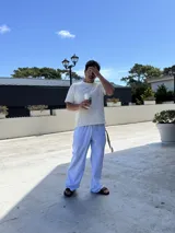 Pantalón de corte ancho y holgado, con diseño de rayas verticales finas en color azul y blanco. Presenta cintura elástica con cordón ajustable y un pequeño bordado en color rojo en la parte superior.