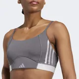Bralette deportivo Adidas Hyperglam color gris oscuro con tirantes finos ajustables. Presenta detalles de costuras curvas y una banda elástica inferior en color blanco con el logo de Adidas.