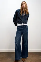 Chaqueta estilo bomber confeccionada en tejido denim de color azul oscuro. Presenta cuello redondo, manga larga, bolsillos delanteros de vivo y cierre frontal con botones ocultos.