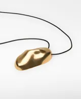 Collar con cordón largo regulable negro y gran dije metálico de forma orgánica con acabado dorado.