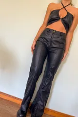 Top negro de cuero sintético con tiras cruzadas en el cuello y abertura en el pecho.