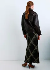 Falda midi de corte al bies con estampado de cuadros escoceses en tonos oscuros, con líneas finas en beige y naranja. Presenta un diseño fluido y ligero.