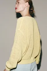 Chaqueta de punto rústico color amarillo claro, con cuello redondo, manga larga y cierre frontal con botones nacarados.