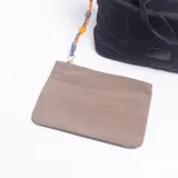Cartera tipo bolso de mano color negro con diseño acolchado de formas redondeadas. Cuenta con doble asa superior, un bolsillo frontal con cierre y un detalle decorativo de cuerda trenzada en color naranja y azul en uno de los laterales.