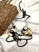 Top de bikini triangular con estampado floral en tonos blanco, negro y dorado. Tiene tiras finas con estampado de lunares blancos sobre fondo negro.