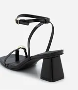 Sandalias negras de tacón ancho, con tiras finas, puntera cuadrada, adorno metálico dorado en el dedo gordo, cierre con hebilla en el tobillo y tacón mediano.