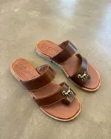 Sandalias de cuero marrón, con diseño de doble tira y detalle de aplique en bronce con forma de perro.