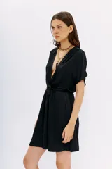 Vestido corto de color negro con escote cruzado, mangas cortas y cintura elastizada. Presenta un diseño de calce relajado y fluido.