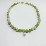 Collar de cuentas de serpentina de 8 mm en tonos verdes, con nudos separadores de hilo verde y un dije central de perla de río natural. Cuenta con broche y terminaciones en acero con baño de oro.