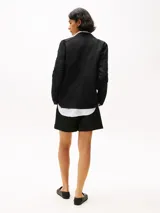 Blazer negro de lino con corte regular, solapas con muescas, botonadura sencilla, bolsillo de parche en el pecho y dos bolsillos delanteros de parche. Forro de algodón.