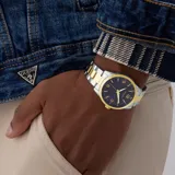 Reloj analógico Guess Easton con caja de 40mm y malla de acero inoxidable bicolor en tonos plateado y dorado. Presenta una esfera azul con acabado sunray, índices y números dorados, y movimiento de cuarzo.