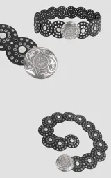 Cinto de cuero negro compuesto por piezas circulares unidas, decoradas con ojales metálicos plateados y apliques circulares grabados. Presenta una hebilla central grande de metal plateado con diseño ornamental grabado.