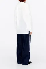 Blusa blanca de viscosa con cuello pico, manga larga y botonadura frontal.