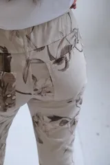 Pantalón de corte recto y ajuste holgado, confeccionado en tela beige con estampado floral en tonos marrones. Presenta cintura elástica con cordón ajustable y ruedos doblados.
