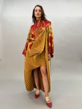Vestido largo plisado con estampado abstracto en tonos rojo, naranja y dorado, cuello alto y mangas acampanadas. Incluye lazo fino para ajustar en la cintura.