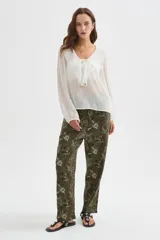Blusa blanca de poliéster con cuello en V, volados frontales y mangas largas con elástico en los puños.