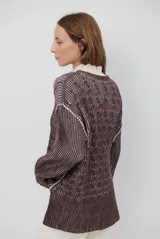 Buzo reversible de tejido de punto con diseño de trenzas, cuello redondo y mangas largas. Presenta una combinación de colores en contraste, con un lado en violeta y el otro en marrón oscuro.