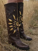 Bota de caña alta color marrón oscuro, confeccionada en cuero, con diseño de sol aplicado en tonos dorados y detalles de tachas metálicas.