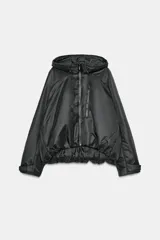 Chaqueta acolchada de color negro con acabado repelente al agua y resistente al viento. Presenta cuello subido con capucha ajustable, cierre frontal con cremallera termosellada, bolsillos delanteros con cremallera y bajo con ajuste elástico. Las mangas largas cuentan con tiras adhesivas ajustables en los puños.