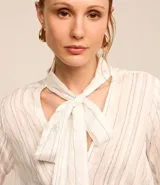 Blusa de crepé color blanco con rayas verticales finas en azul. Tiene cuello con lazo para atar, mangas largas y corte recto.