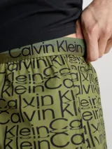 Conjunto de pijama Calvin Klein compuesto por una remera negra de cuello redondo con logo estampado en el pecho y un short verde con estampado tipográfico de la marca.