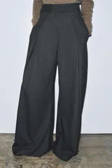 Pantalón wide leg gris oscuro con raya diplomática, tiro medio, bolsillos laterales ocultos, pinzas delanteras y cierre frontal con cremallera, botón y ganchos metálicos.