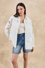 Sobrecamisa blanca de algodón con bordados florales calados en mangas, cuello y pechera. Corte oversize, manga larga y dos bolsillos frontales.