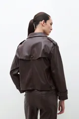 Trench corto color chocolate de cuero sintético, con doble botonadura, cuello alto y charreteras en los hombros.