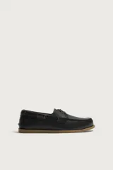 Zapato náutico de piel color negro, con cordones y suela plana de goma marrón en contraste.