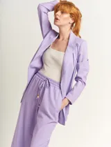 Blazer oversized lila de corte recto, largo a la cadera, con hombreras finas forradas, costuras internas con sesgo combinado y maxi bolsillos delanteros. Incluye lazo de algodón con detalle a tono.