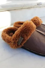 Pantufla de cuero color habano con interior de piel sintética, suela de goma y detalle de costura central.