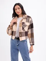 Sobrecamisa de corte cropped con diseño a cuadros en tonos rosa y beige. Presenta cuello clásico, cierre frontal con botones metálicos, mangas largas con puños abotonados y dos bolsillos frontales con solapa.