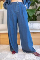 Pantalón de denim azul de calce relajado y fluido, decorado con pequeñas perlas aplicadas en toda la superficie con mayor densidad en el ruedo. Presenta pinzas frontales, bolsillos laterales y cierre de botón.