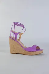Sandalias de plataforma con taco corrido revestido en yute, confeccionadas en cuero color lila. Presentan diseño de puntera abierta y tiras largas para atar alrededor del tobillo.