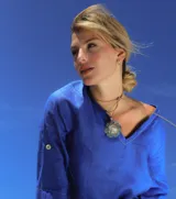 Collar con dije dorado en forma de flor con incrustaciones de perlas, con tiras de cuero sintético color beige que se atan al cuello.