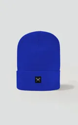 Gorro de tejido liso color azul eléctrico, con borde doblado y un pequeño parche cuadrado negro con un logo bordado en blanco que simula unas tijeras cruzadas.