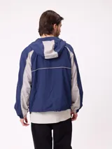 Rompevientos Rusty con capucha, diseño bicolor en azul marino y gris, cierre frontal y logo bordado en el pecho.