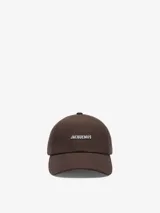 Gorra de visera marrón con el logotipo de Jacquemus en letras metálicas plateadas en la parte frontal y visera pespunteada.
