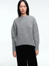 Sweater de tejido de punto con textura suave y acabado ligeramente afelpado, de corte holgado, cuello redondo y mangas largas con puños ajustados.