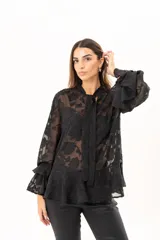 Blusa negra de tejido semitransparente con diseño floral en relieve, cuello alto con lazo frontal y mangas largas con volados en los puños.